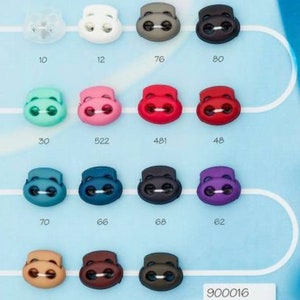 Puede incluir: Surtido de topes de cord&oacute;n de pl&aacute;stico en varios colores, incluyendo blanco, gris, verde, rosa, rojo, azul, morado, marr&oacute;n y negro. Cada tope de cord&oacute;n tiene dos agujeros y un n&uacute;mero &uacute;nico impreso debajo. Los n&uacute;meros van del 10 al 80, del 30 al 70 y del 48 al 68. El texto "900016" est&aacute; impreso en la esquina inferior derecha.