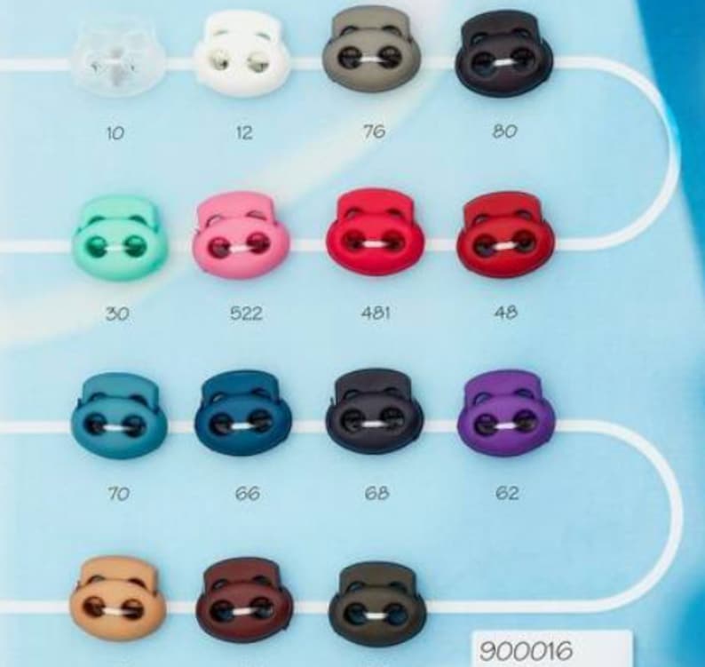 Puede incluir: Surtido de topes de cord&oacute;n de pl&aacute;stico en varios colores, incluyendo blanco, gris, verde, rosa, rojo, azul, morado, marr&oacute;n y negro. Cada tope de cord&oacute;n tiene dos agujeros y un n&uacute;mero &uacute;nico impreso debajo. Los n&uacute;meros van del 10 al 80, del 30 al 70 y del 48 al 68. El texto "900016" est&aacute; impreso en la esquina inferior derecha.