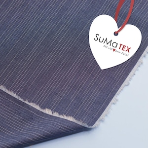 Könnte beinhalten: Nahaufnahme eines marineblauen Stoffes mit feinen weißen Streifen. Der Stoff hat einen rohen Rand. Ein weißes herzförmiges Etikett mit dem Text "SuMaTEX" und "Mit viel zum Detail" ist mit einem roten Band befestigt.