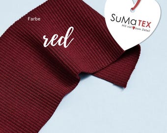 May include: Red ribbed fabric with the word "red" and the text "Farbe" written on it. A heart-shaped tag with the text "SUMATEX Mit viel zum Detail" is attached to the fabric.