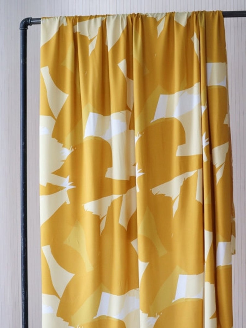 May include: Yellow fabric with a white abstract pattern. The fabric has a soft, flowing drape.