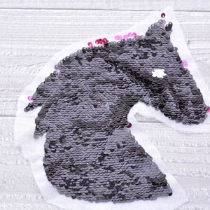 Może przedstawiać: Czarna aplikacja głowy konia wykonana z cekinów. Cękiny są ułożone w wzór, który tworzy kształt głowy konia. Aplikacja znajduje się na białym tle.