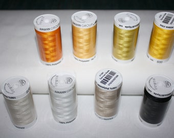 Può includere: Otto rocchetti cilindrici di filo da ricamo 100% poliestere Amann Group Poly Sheen disposti su due file. I colori includono arancione, oro, giallo, beige chiaro, bianco, beige e nero, ciascuno con un'etichetta superiore bianca con testo.