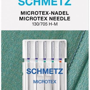 Könnte beinhalten: Eine Packung mit fünf silbernen Nähnadeln mit der Aufschrift "Schmetz Microtex 130/705 H-M". Die Nadeln sind in einem durchsichtigen Kunststoffgehäuse mit einem weißen Etikett verpackt. Das Etikett enthält auch die Größe jeder Nadel, die von 60 bis 80 reicht.