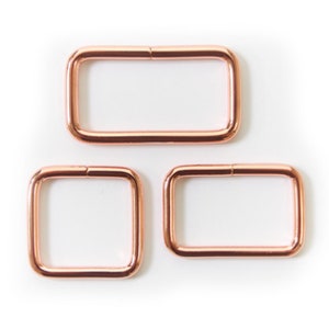 Peut inclure: Trois anneaux en D en métal rose gold de différentes tailles. Les anneaux en D sont tous lisses et brillants.