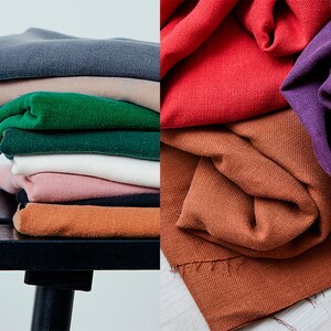 May include: A stack of folded fabric in various colors, including gray, tan, green, white, pink, black, and orange. The fabric is arranged on a black bench. Additional fabric in red, orange, and purple is also displayed.