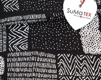 May include: Black and white fabric with a geometric pattern. The fabric is folded in half and a heart-shaped tag is attached to the fabric. The tag is white with black text that reads "SUMATEX Mit viel zum Detail".