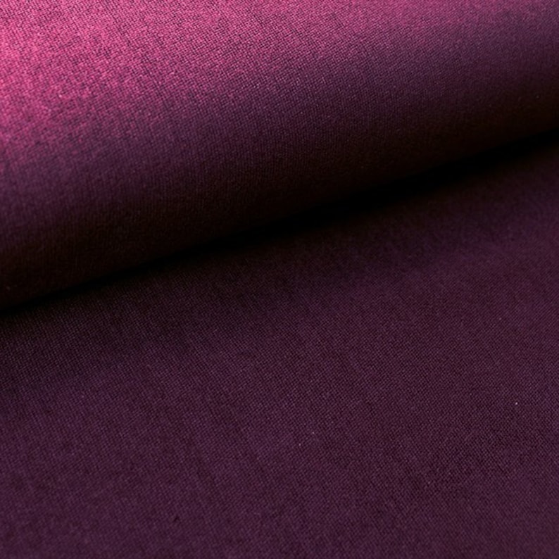 Peut inclure: Gros plan sur un tissu violet fonc&eacute; avec une texture subtile. Le tissu est pli&eacute; en deux, montrant la surface lisse sur le dessus et la surface textur&eacute;e sur le dessous.