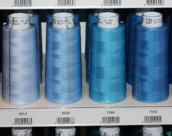 Può includere: Primo piano di dieci bobine di filo in diverse tonalità di blu. Le bobine sono disposte in fila su uno scaffale. Le bobine sono etichettate con numeri e il testo "120 m x 100".