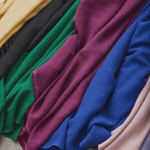 Könnte beinhalten: Eine Auswahl an Tencel-Stoffen in verschiedenen Farben: Gelb, Schwarz, Grün, Lila, Blau und Rosa. Die Stoffe haben ein feines, strukturiertes Muster und sind drapiert, um ihren Fall zu zeigen. Das Bild enthält den Text "Tencel" und "OEKO-TEX".