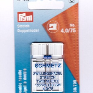 May include: A packet of Schmetz twin needles for stretch fabrics. The packaging is blue and orange, with the Prym logo and text in multiple languages. The needles are size 4.0/75, suitable for sewing stretch materials.