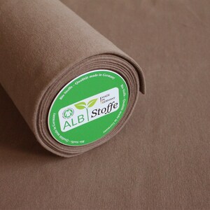 Könnte beinhalten: Eine Rolle braunen Stoffes mit einem grünen Etikett, auf dem "ALB Stoffe" und "Made in Germany" steht.