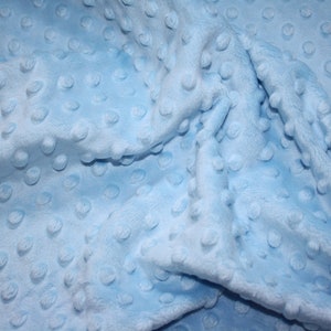 Könnte beinhalten: Nahaufnahme eines hellblauen Stoffes mit strukturierter, genoppter Oberfläche. Der Stoff hat ein weiches, plüschiges Aussehen mit einem Muster aus gleichmäßig verteilten, erhabenen Punkten. Das Wort "SuMaTex" ist in der oberen linken Ecke sichtbar.