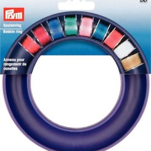 Pode incluir: Anel de carretel de plástico roxo para guardar carretéis de fio. O anel tem 12 ranhuras para carretéis e é etiquetado como "Spulenring Bobbin ring".