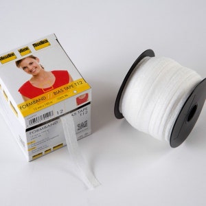 Könnte beinhalten: Weißes Schrägband auf einer schwarzen Spule neben einer Schachtel mit der Aufschrift "FORMBAND BIAS TAPE T12". Die Schachtel zeigt eine Frau in einem roten Oberteil und den Text "12 mm x 100 m". Das Band ist 1,2 cm breit.