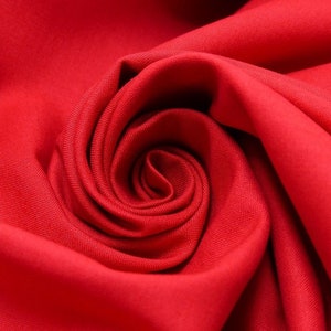 Könnte beinhalten: Nahaufnahme eines roten Stoffes, der zu einer Rosenform gefaltet ist. Der Stoff ist glatt und hat eine weiche Textur.