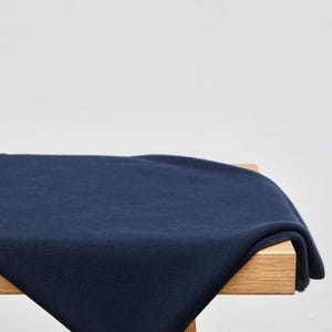 May include: A navy blue fabric draped over a light-colored wooden surface. The fabric is folded, creating soft shadows and texture. The background is a plain white.