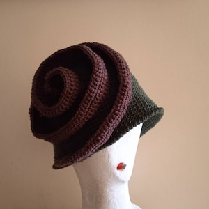 May include: A brown and green crocheted hat shaped like a rose. The hat is on a white mannequin head.