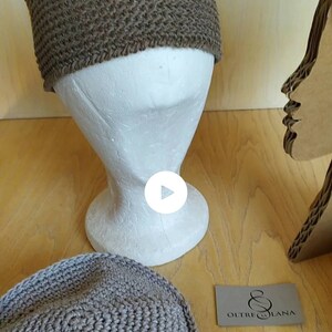 May include: Two brown crocheted hats on a mannequin head and a wooden surface. The hats are made with a thick yarn and have a simple design. The text "OLTRE LA LANA" is visible on a small card.