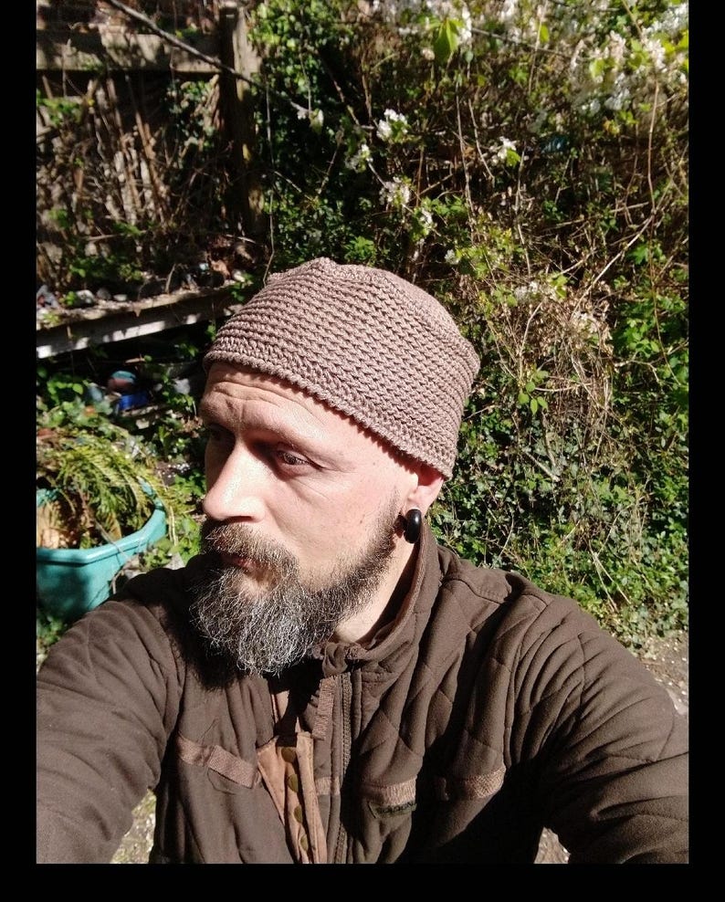 May include: A brown knitted beanie with a textured pattern. The beanie is worn by a person with a beard and a brown jacket.