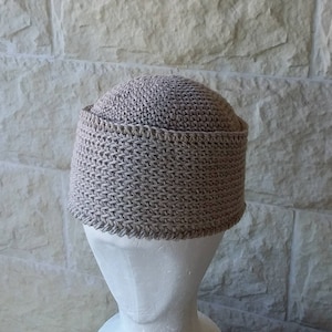 May include: A beige crocheted hat with a wide brim. The hat is made with a textured stitch and has a simple design.