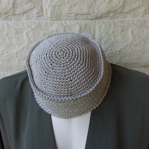 May include: A grey crocheted kippah, a traditional Jewish head covering, is shown on a grey jacket.