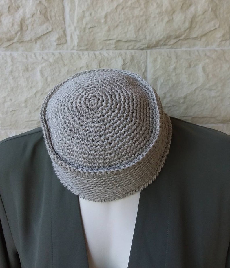 May include: A grey crocheted kippah, a traditional Jewish head covering, is shown on a grey jacket.