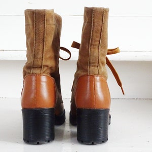 May include: A pair of brown suede ankle boots with a chunky heel and laces. The boots have a brown leather lower section and black soles.