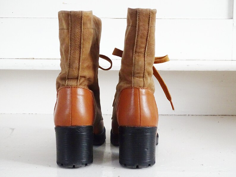 May include: A pair of brown suede ankle boots with a chunky heel and laces. The boots have a brown leather lower section and black soles.
