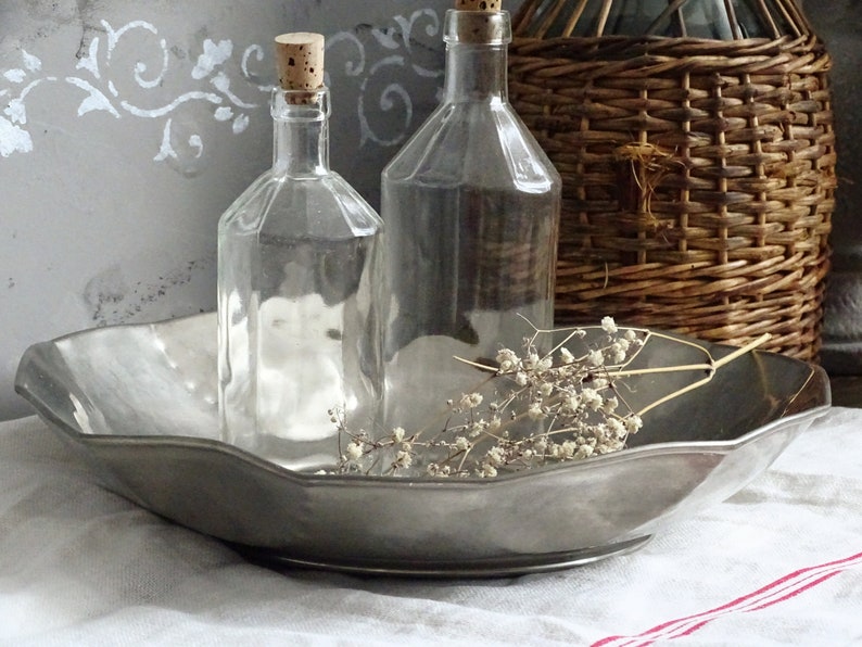 May include: A silver serving tray with a scalloped edge, holding two clear glass bottles with cork stoppers and a sprig of dried white flowers.