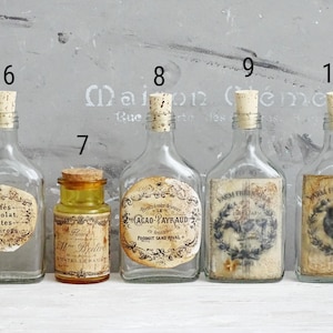 Puede incluir: Cinco botellas de vidrio numeradas 6, 7, 8, 9 y 10. Cuatro son de vidrio transparente con tapones de corcho y etiquetas de papel estilo vintage. Una es un frasco de vidrio &aacute;mbar m&aacute;s peque&ntilde;o con tap&oacute;n de corcho y etiqueta con texto.