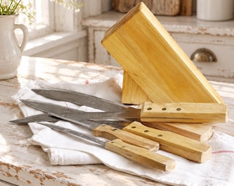 May include: A set of four kitchen knives with light-colored wooden handles and silver-toned metal blades, resting on a white cloth next to a matching wooden knife block. The knives feature three visible rivets on each handle.