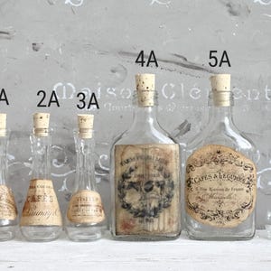 Puede incluir: Seis botellas de vidrio transparente con tapones de corcho, etiquetadas del 1A al 6A. Las botellas 1A, 2A, 3A y 6A son delgadas con cuellos estrechos. Las botellas 4A y 5A son m&aacute;s anchas con etiquetas rectangulares y redondas con texto negro.