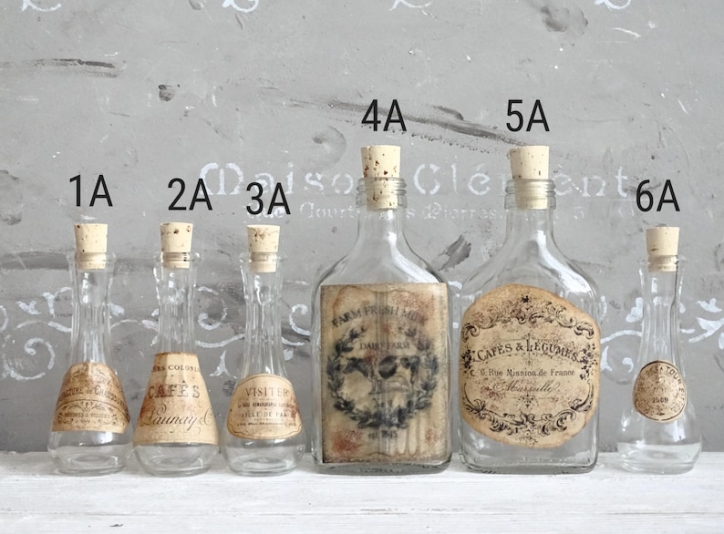 Puede incluir: Seis botellas de vidrio transparente con tapones de corcho, etiquetadas del 1A al 6A. Las botellas 1A, 2A, 3A y 6A son delgadas con cuellos estrechos. Las botellas 4A y 5A son m&aacute;s anchas con etiquetas rectangulares y redondas con texto negro.