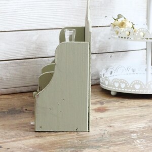 May include: A distressed, sage green wooden organizer with multiple compartments. A small, clear glass container sits in the top section. The organizer has a rustic, vintage aesthetic, perfect for home decor or storage.
