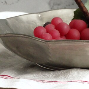 May include: A silver serving bowl with a scalloped edge, filled with a cluster of pink grapes.