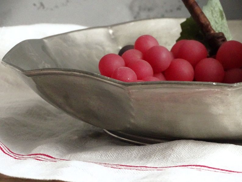 May include: A silver serving bowl with a scalloped edge, filled with a cluster of pink grapes.