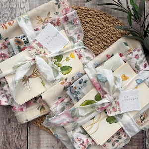 May include: Two bundles of cream-coloured fabric featuring floral patterns, tied with frayed white ribbon. Each bundle includes a botanical illustration card with the text "be creative" and raw-edged fabric scraps in shades of pink, green, and blue.