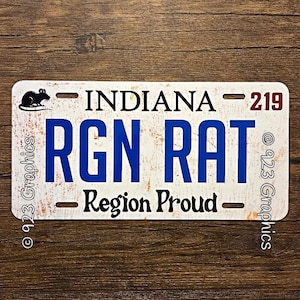 Puede incluir: Placa de matrícula blanca con texto azul "RGN RAT" y "Region Proud". La palabra "INDIANA" está en la parte superior, con el número "219" en rojo. Una silueta de rata negra está a la izquierda.