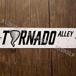May include: White metal sign with black text that reads "Tornado Alley" with a black and white illustration of a tornado.