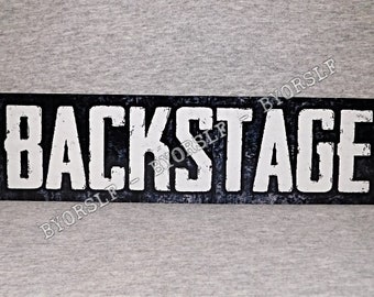 May include: Black and white sign with the word "BACKSTAGE" in white letters on a black background. The sign has a distressed, vintage look.