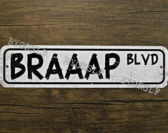 May include: A white metal sign with black text that reads "BRAAAP BLVD". The sign has a distressed, vintage look.