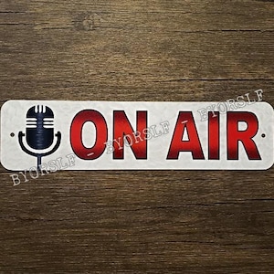 May include: White metal sign with a red gradient that says "ON AIR" with a black microphone icon on the left side.
