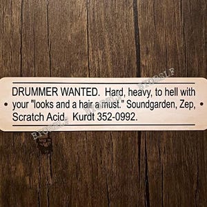 May include: A gold-colored metal sign with black text that reads "DRUMMER WANTED. Hard, heavy, to hell with your "looks and a hair a must." Soundgarden, Zep, . Scratch Acid. Kurdt 352-0992."