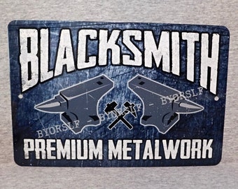 May include: A rectangular metal sign with a distressed blue background. The word "BLACKSMITH" is in large white letters at the top. Below are two anvil illustrations and the words "PREMIUM METALWORK" in white. The sign has two small holes.