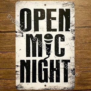 May include: White metal sign with black text that reads "Open Mic Night". A microphone icon is between the words "Mic" and "Night".