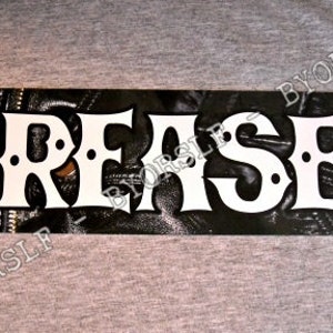 May include: Black and white metal sign with the word "Greaser" in white letters on a black background. The background is a faux leather texture.