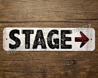 May include: White metal sign with black text that reads "STAGE" and a red arrow pointing to the right. The sign has a distressed, vintage look.