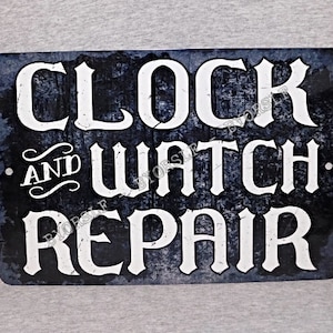May include: Black and white metal sign with the text "Clock and Watch Repair" in a vintage style font.