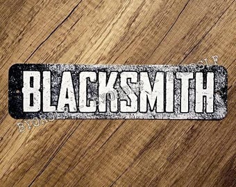 May include: Black and white metal sign with the word "BLACKSMITH" in white letters on a black background. The sign has a distressed, vintage look.
